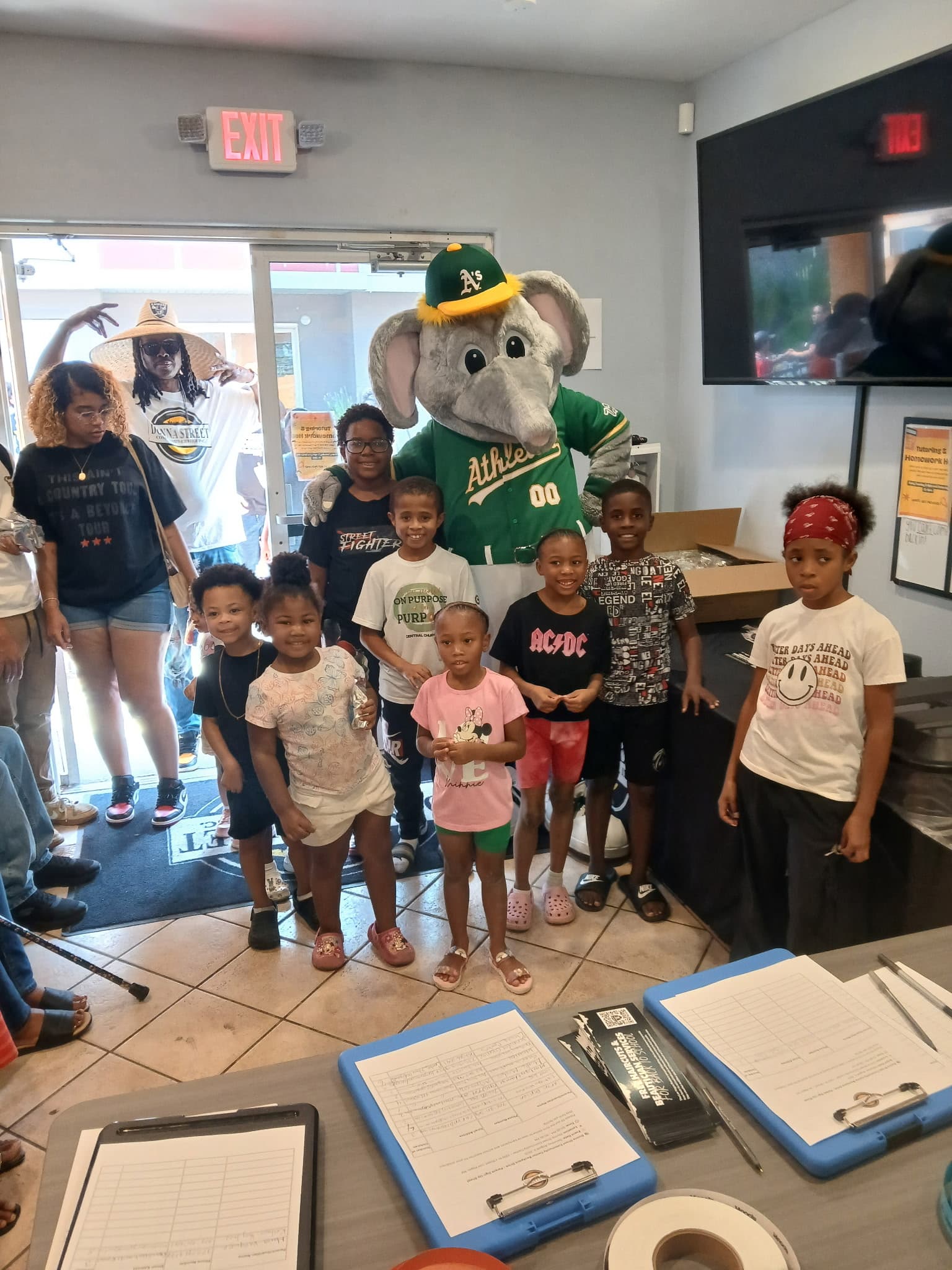 Children and adults posing with the Oakland Athletics elephant mascot in a community center.